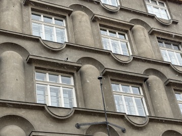 Zaoblené polosloupy a buřtíkové římsy na fasádě domu v Kamenické 35
